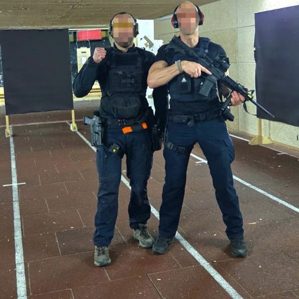 Deux hommes en tenue d'intervention et casques antibruit posant dans un stand de tir, l'un tenant une carabine